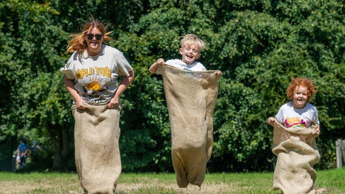 A woman and two children enjoying a sack race in sunny countryside